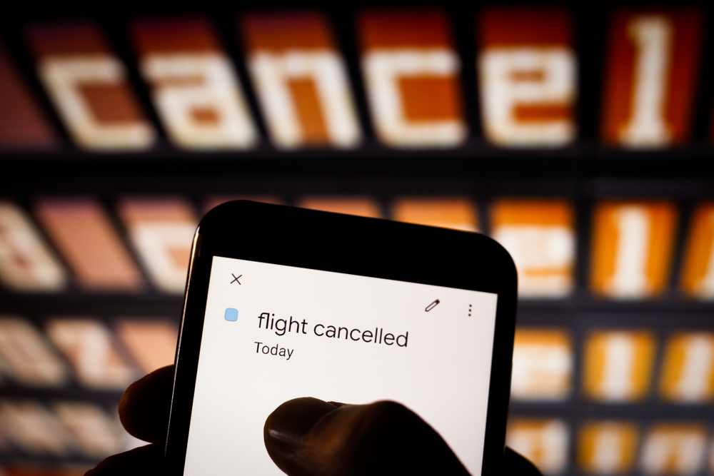 Phone showing flight canceled in front of canceled airport status screen for a frequently asked questions section on how much does travel insurance cost