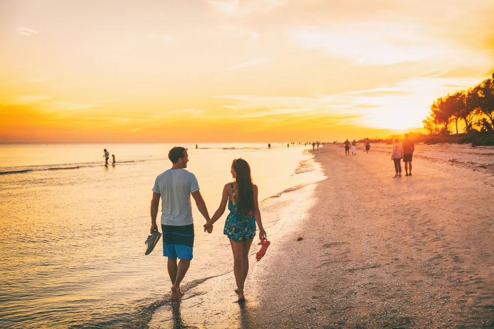 Two people walking along the white sand beach in Sanibel during the best time to visit and holding hands