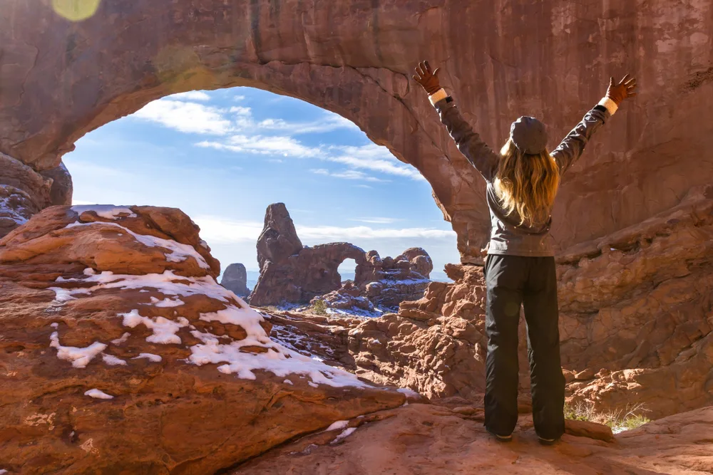 Woman holding her arms up while standing inside the Turret Arch during the winter, the worst time to visit Moab