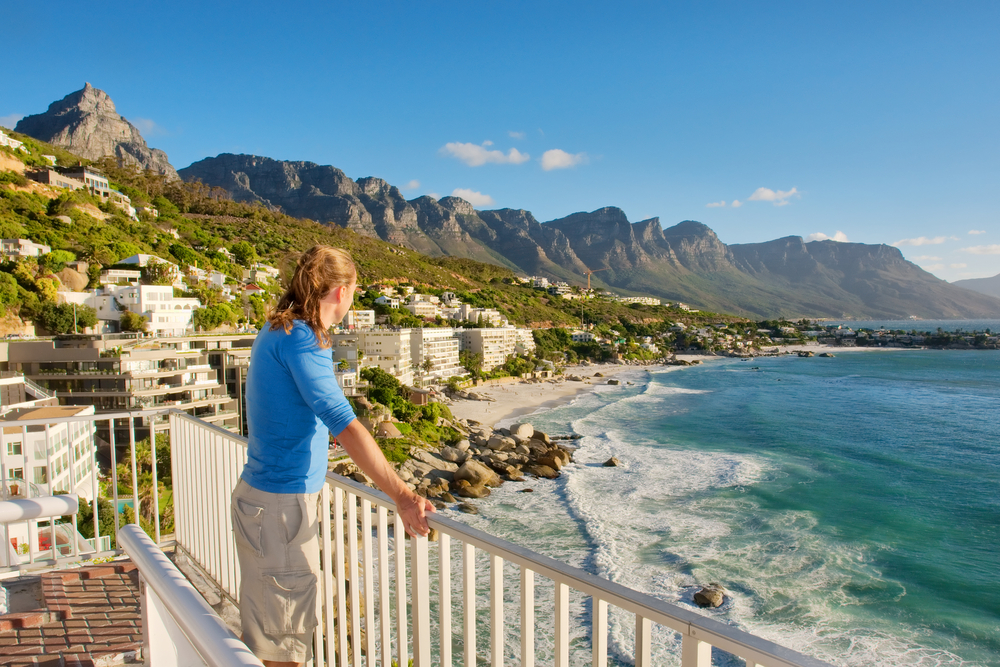 Young man in a blue shirt with long hair holds the railing of his hotel and looks out over the ocean for a piece titled Is Africa Safe to Visit