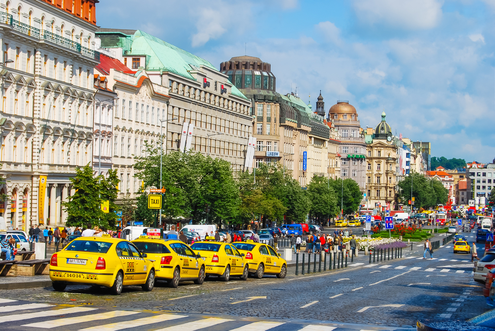 A bunch of yellow taxis at the taxi stand outside of a historical building for a piece on Is Prague Safe to Visit