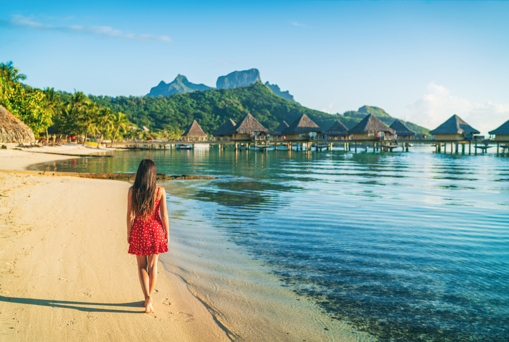 Woman walking along a gorgeous white sand beach in Bora Bora during the best time to visit French Polynesia