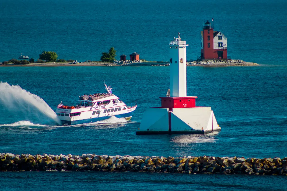 Image of a high-speed ferry spraying water out of the back while passing between two lighthouses in the Mackinac Island harbor