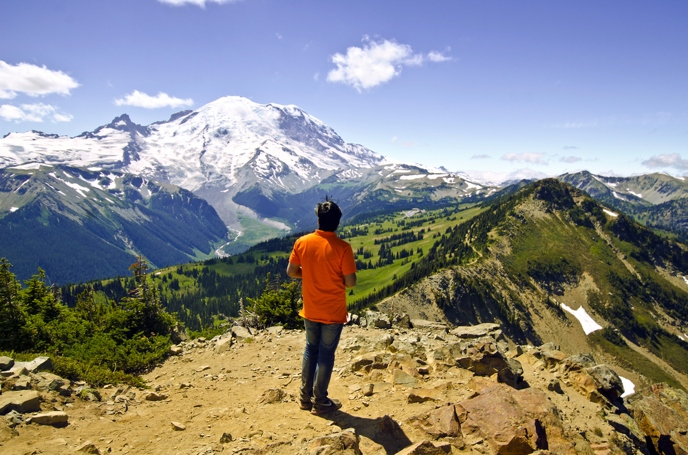 Guy hiking Mount Rainier and overlooking the valley below from Dege Peak