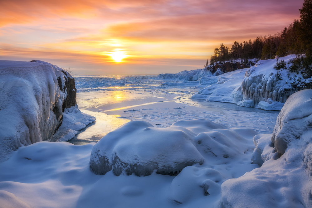 Frozen Lake Michigan pictured during the worst busy time to visit the Upper Peninsula with snow-capped rocks and ice on the coast of the water