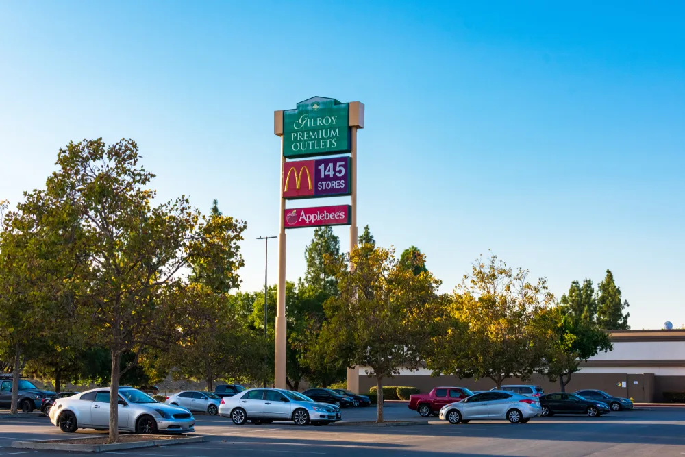 Sign that reads Gilroy Premium Outlets pictured with a McDonalds sign below and cars in the parking lot