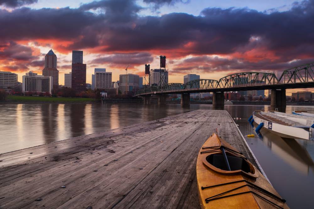 Panorama of the skyline with pink clouds and a bridge in the background with a kayak in the foreground pictured for a piece on the best places to visit in the United States