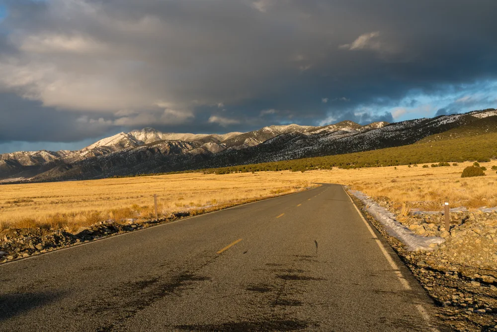 Road leading to the mountains during the winter during the worst time to visit Great Sand Dunes National Park with storm clouds on the horizon above the mountains