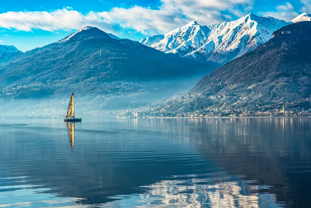 Sailboat on Lake Como during the overall cheapest time to visit with snow-capped mountains in the background