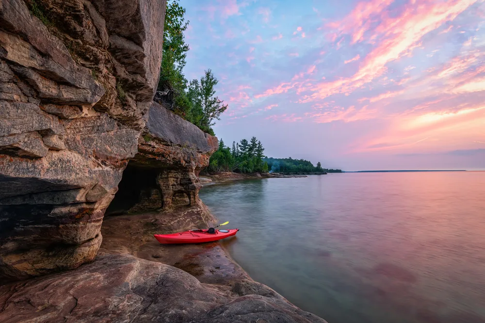 Kayaker on Lake Superior by the caves during sunset, pictured during the best time to visit the Upper Peninsula