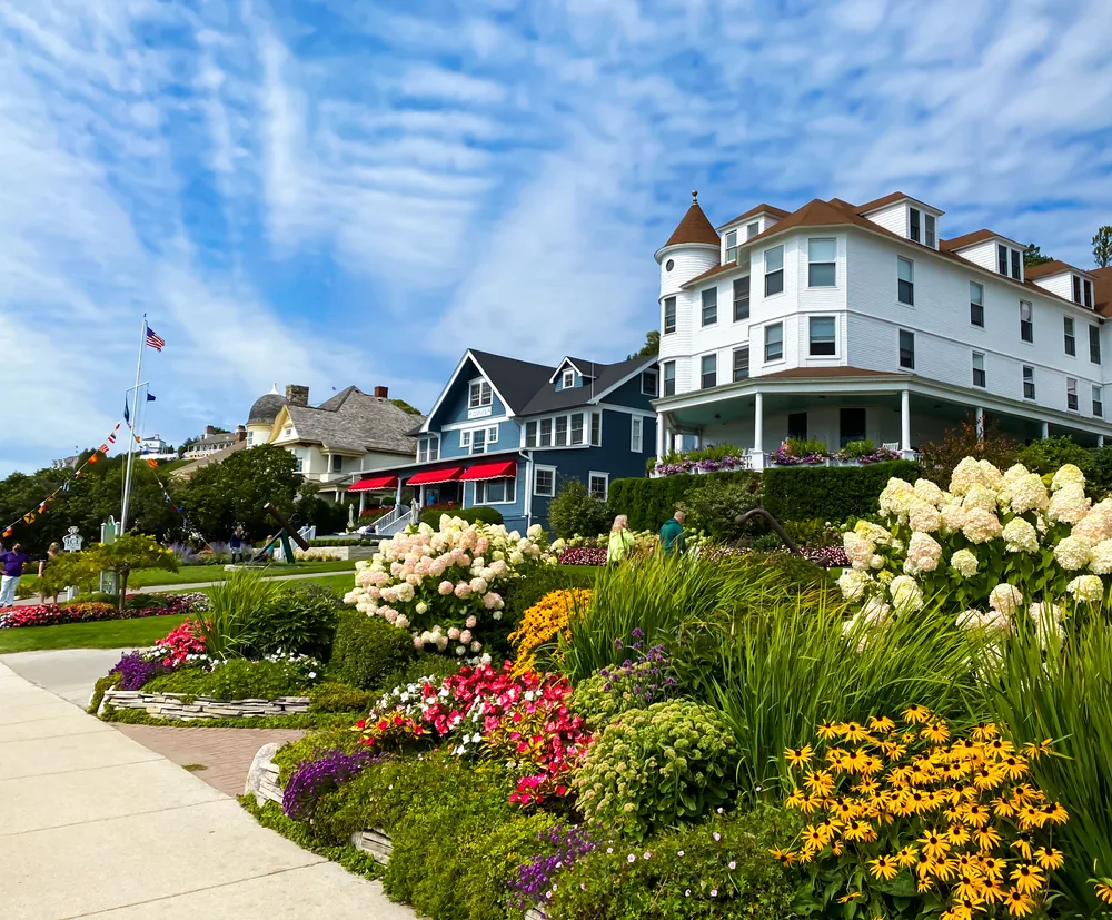 Gorgeous blue skies with a bit of high-level clouds in the above an older-style home with gorgeous flowers in front, pictured during the worst time to visit Mackinac Island
