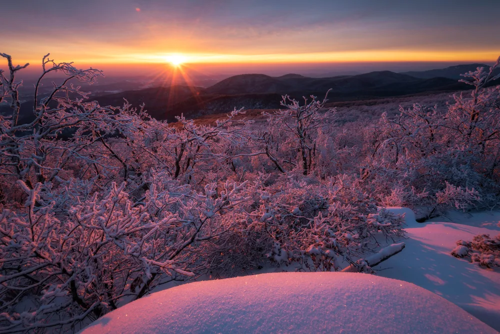 Sun rises over the snow-capped mountains and trees during the winter, the worst time to visit Shenandoah National Park