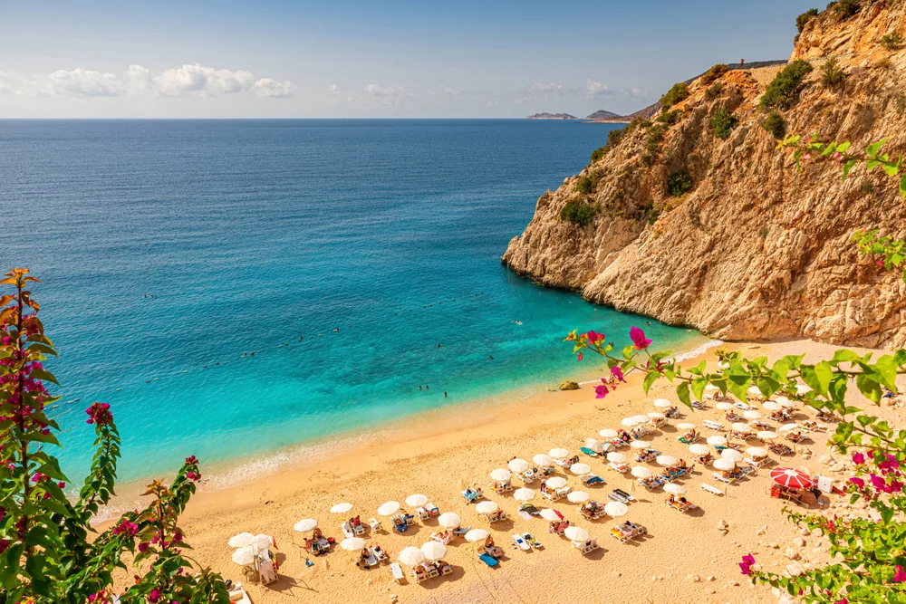 Beige sand beach between the tall rocky coastline with teal water lapping the beach in Antalya, one of the best places to visit in Turkey