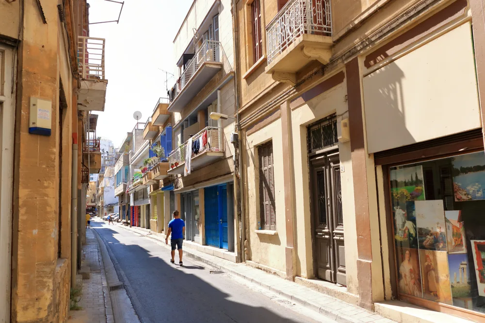 For a post on whether or not Cyprus is safe to visit, a man walks down the street in a blue shirt between gorgeous old buildings