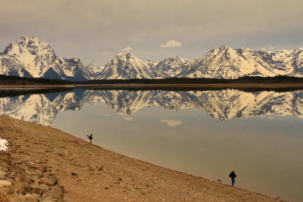 Two men fishing in the Teton's National Park lake during the late fall, one of the best times to visit Jackson Hole Wyoming
