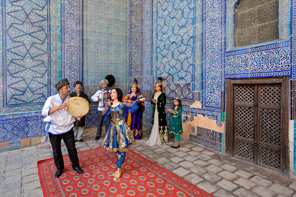 People standing outside of a blue mosque with gorgeous tiled walls with a red rug below them