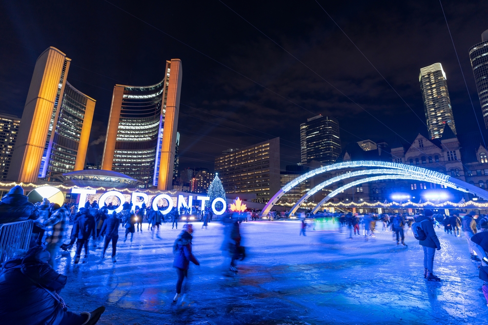 People in Nathan Phillips Square pictured ice skating at night during cheapest time to visit Toronto with lights all around