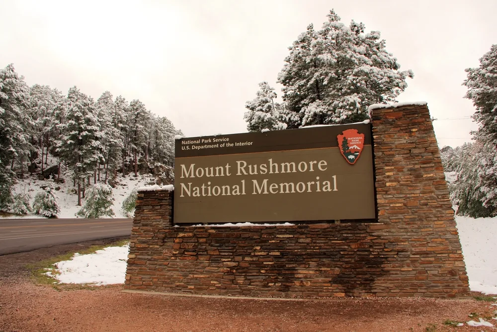 Snow on the ground around the entrance sign to Mount Rushmore pictured in the winter, the cheapest time to visit the monument