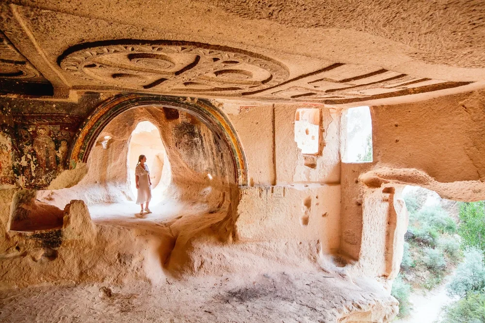Woman in a white dress walking through a cave with old markings on it during the best time to visit Cappadocia