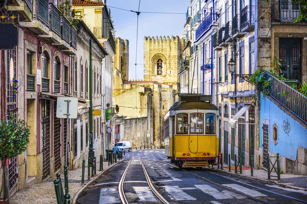 The famous yellow tram in Lisbon (pictured during the best time to visit) driving through the shadows in the middle of the narrow city streets