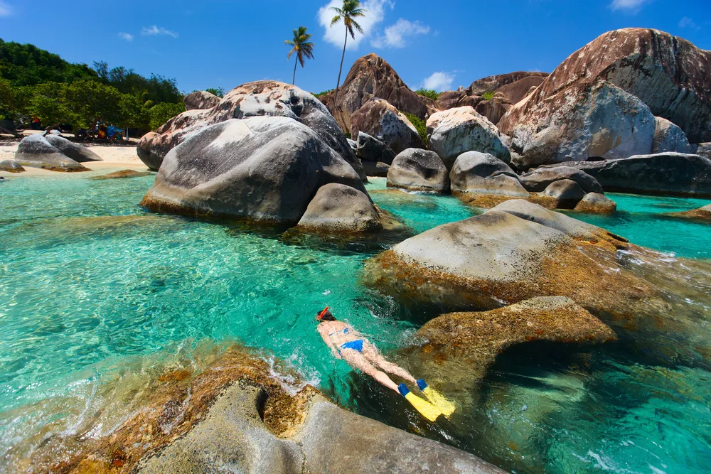 Woman in a blue bikini snorkeling through a big rock formation at one of the best resorts in the Virgin Islands