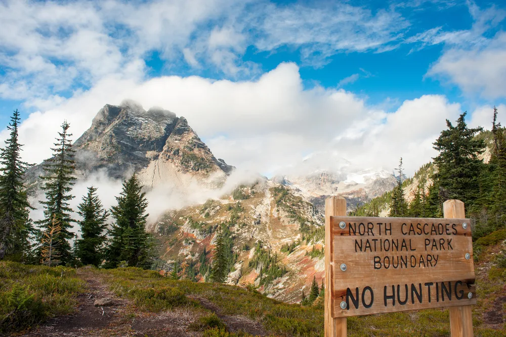 Clouds over a mountain with a sign that says North Cascades National Boundary pictured during the best time to visit the park