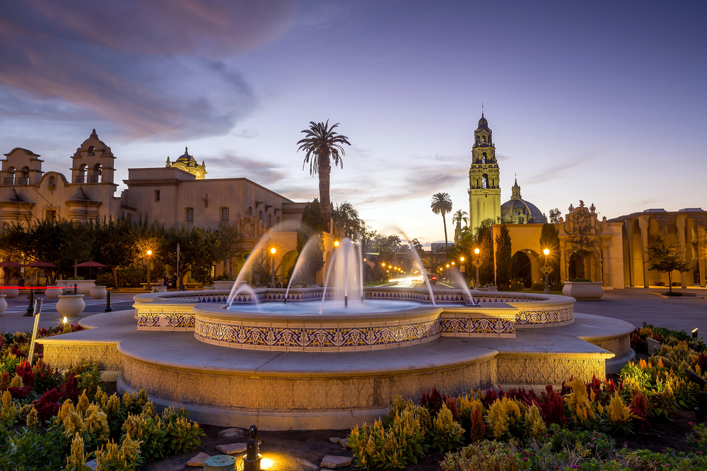 Dusk view of Balboa Park pictured with lights behind the water in the fountain and lighting up the street by the stucco buildings