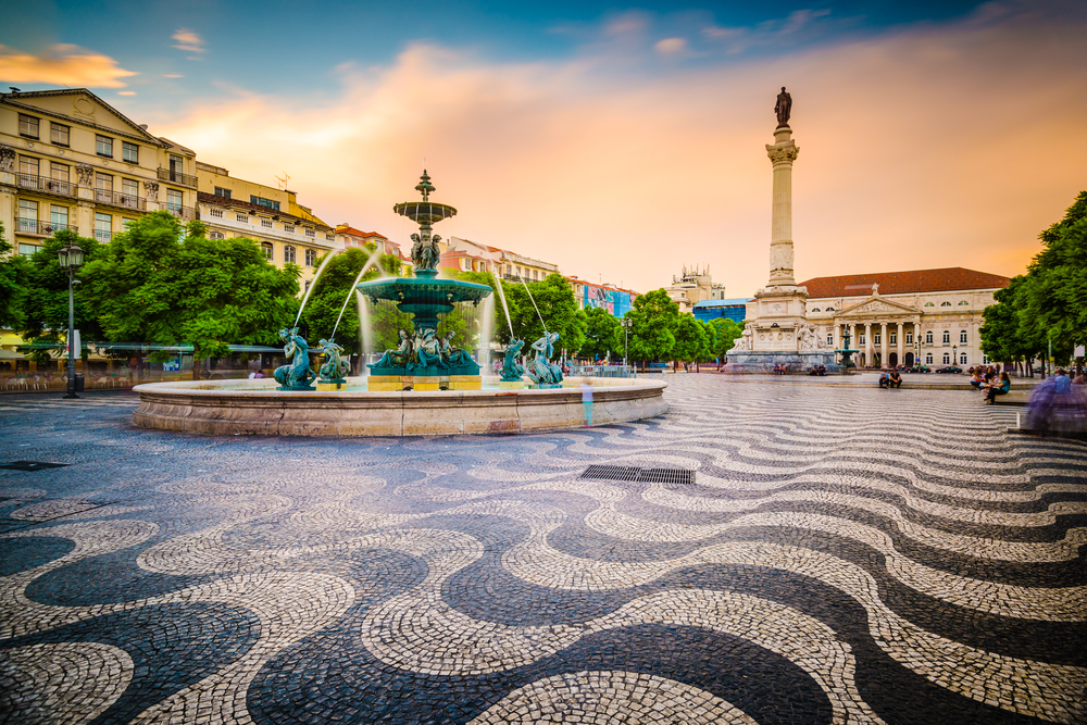 Rossio Square pictured during the cheapest time to visit Lisbon with a fountain in the middle of the wavy-style mosaic floor