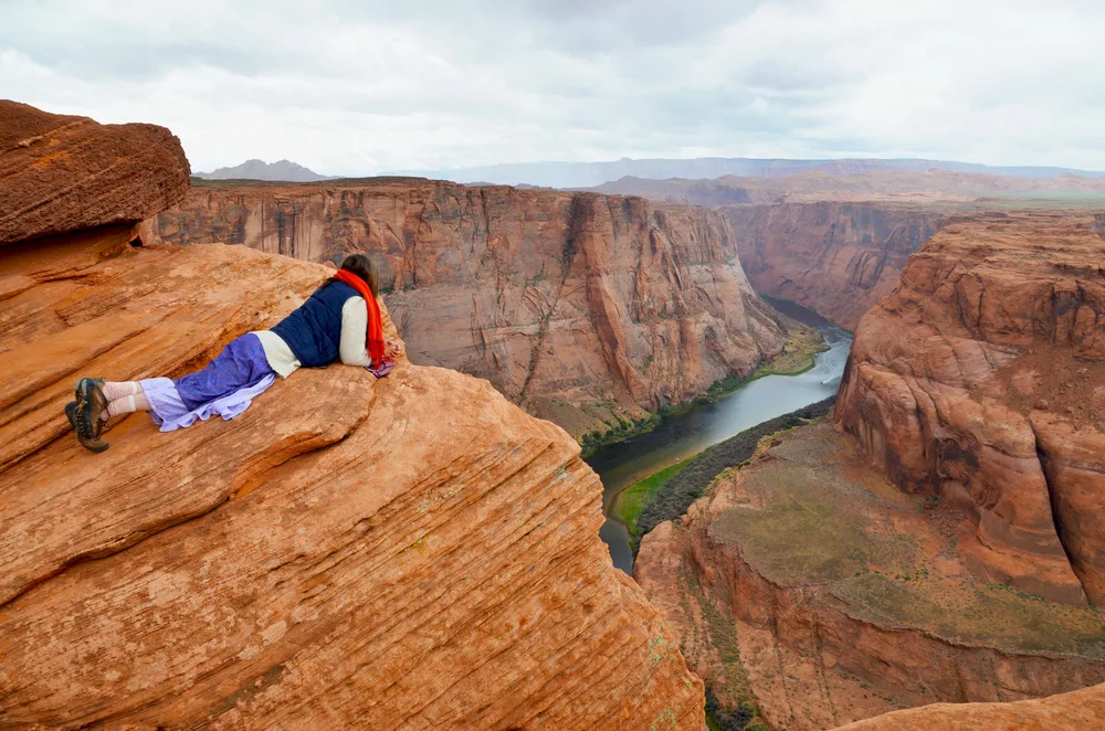 Woman in a Mennonite-style dress lying face down on the rocks overlooking Horseshoe Bend