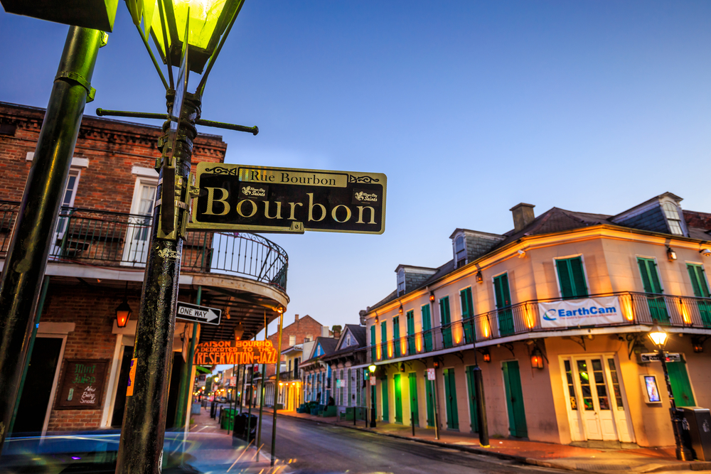 Bourbon Street sign pictured at night with lights shining up on the buildings