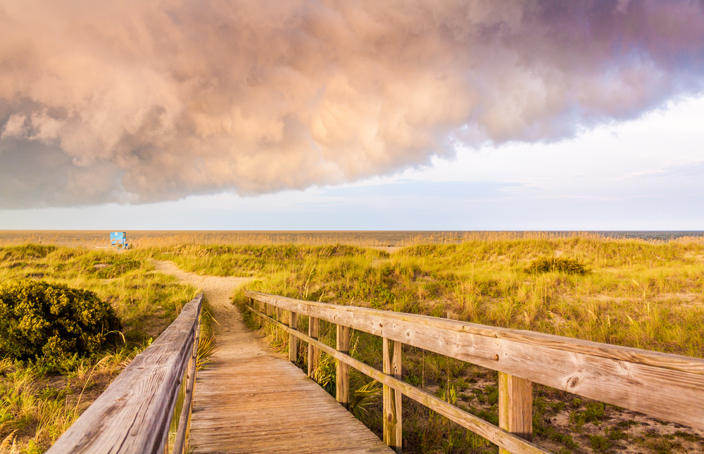 Walkway to the beach with prairie grass all around with storm clouds overhead pictured during the worst time to visit Tybee Island