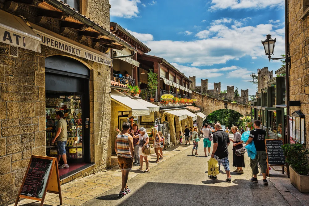 For a piece titled Is San Marino Safe to Visit, a bunch of tourists shop in an open-air market