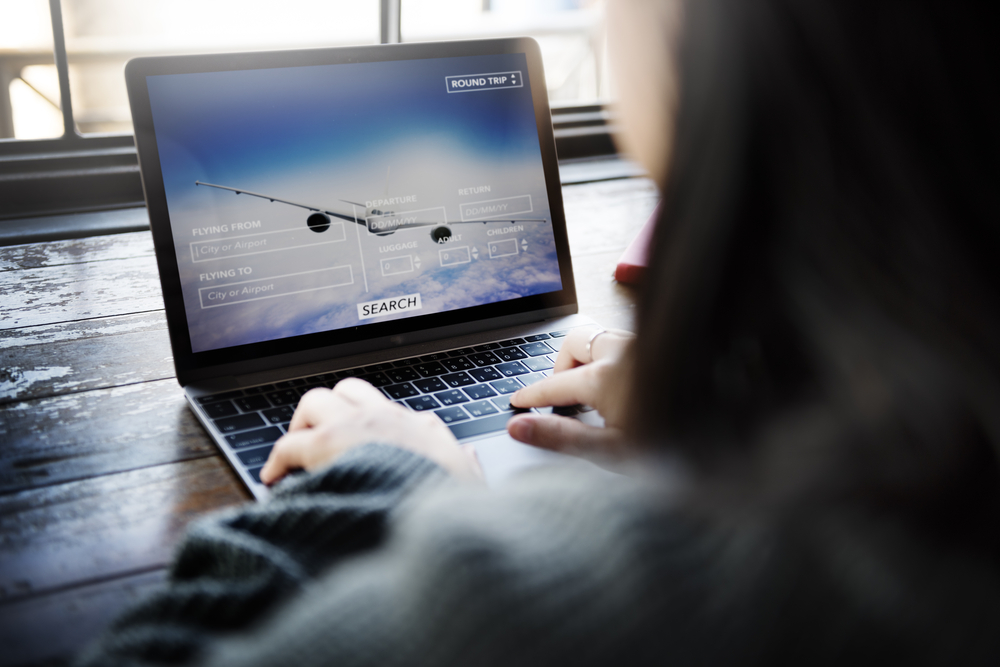 Woman sits in front of laptop computer booking a flight for a piece on the cheapest days to fly
