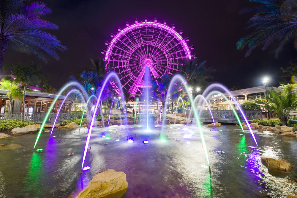 Orlando Eye in the background of a splash pad with water that's lit up at night
