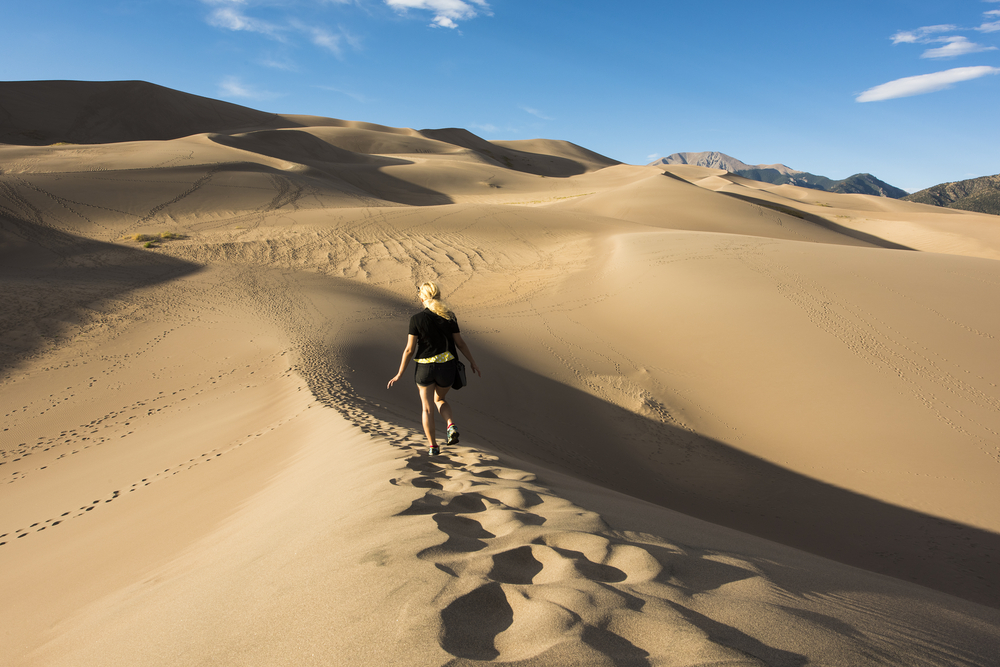 Woman in shorts and a short-sleeved black shirt walking along the top of a sand dune during the best time to visit the Great Sand Dunes National Park