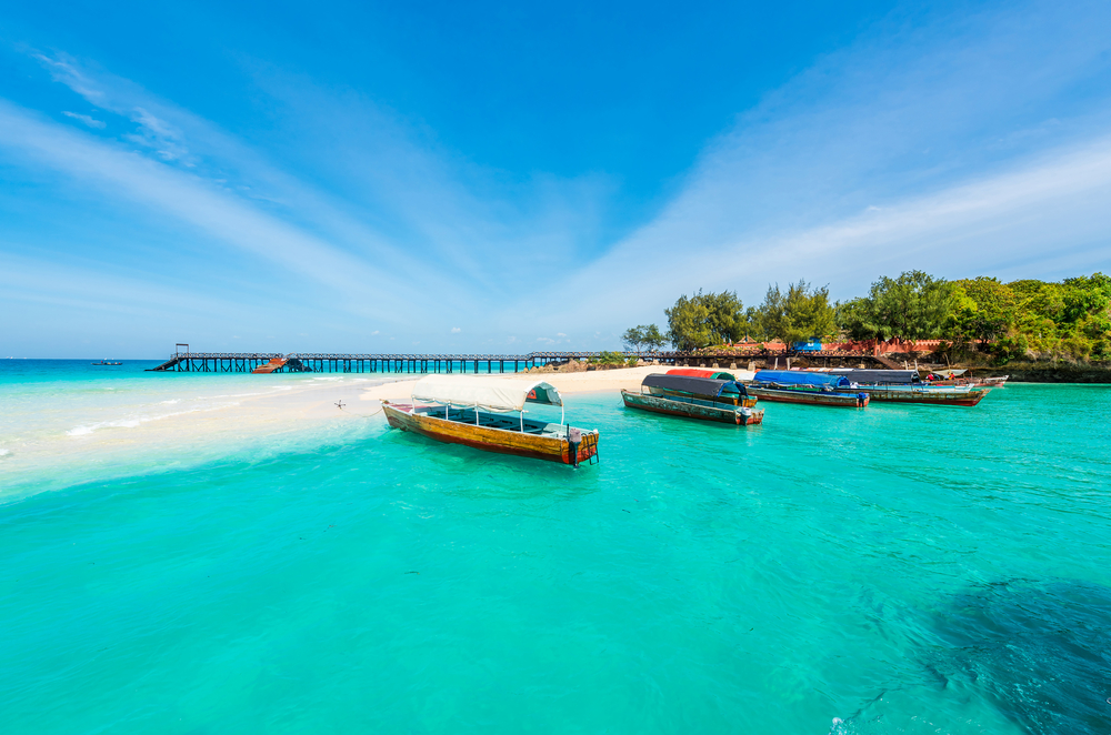 Boats moored on the crystal-clear water off the white sand beach of Zanzibar, pictured during the best time to visit