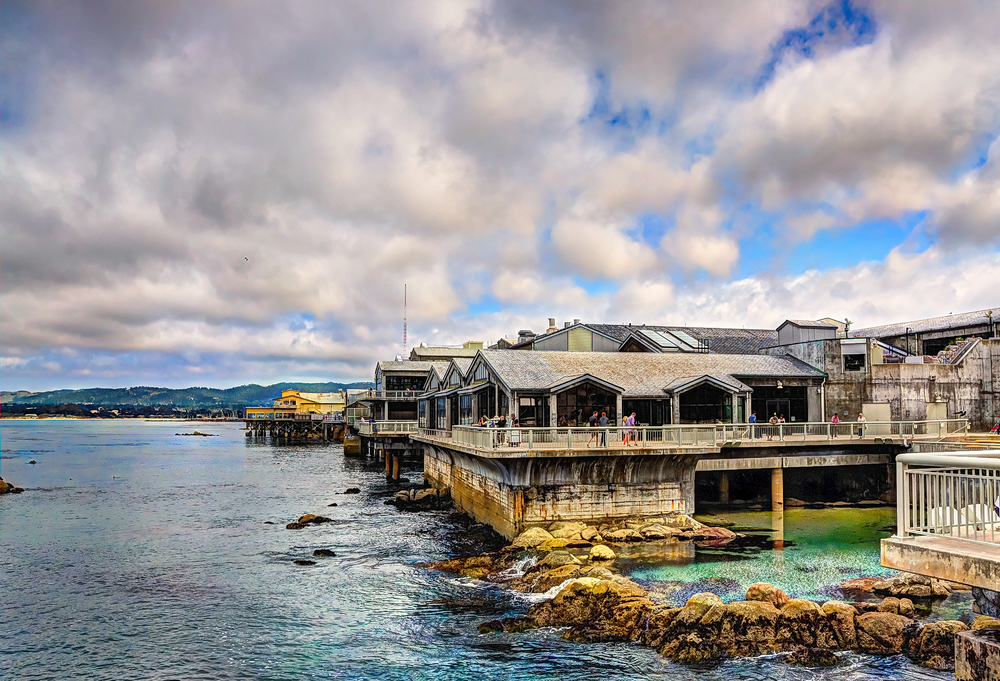 Exterior view of the Monterey Bay Aquarium on a cloudy day with an image of it on a pier overlooking the water
