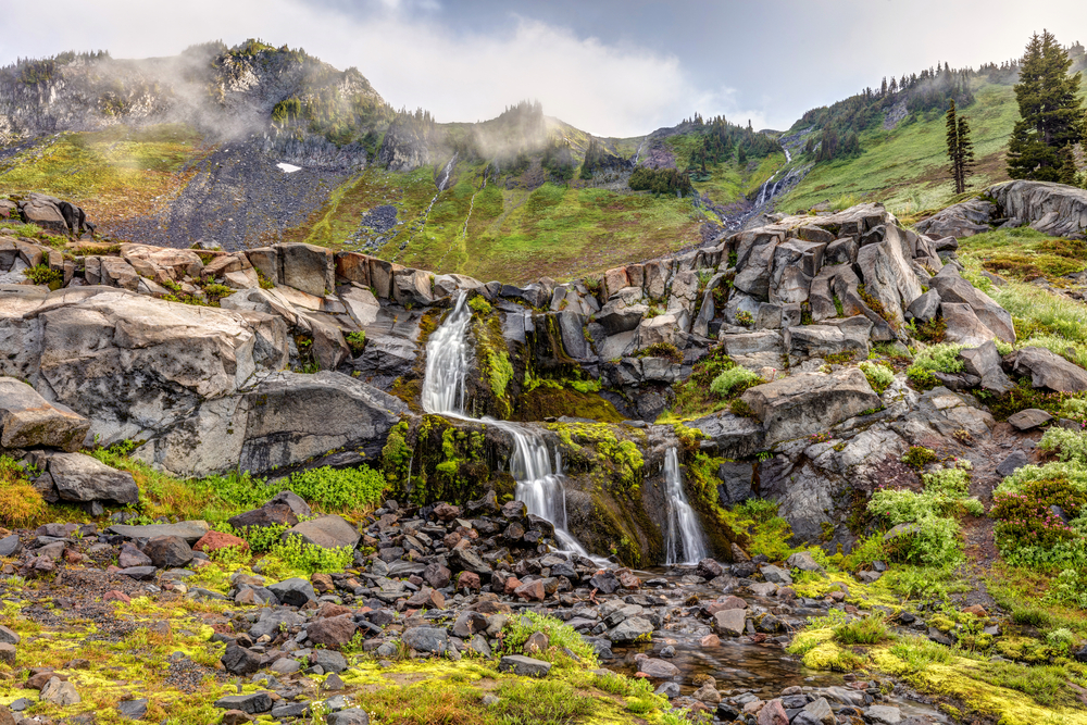 Gorgeous waterfall with a stream cascading down the hillside between moss-covered rocks during the best time to visit Mount Rainier, the spring