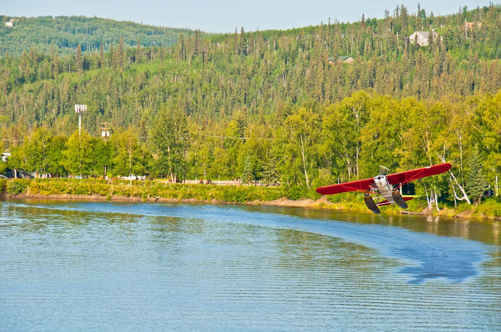 Red and white seaplane taking off from the water in Fairbanks during the summer, the best time to visit the city