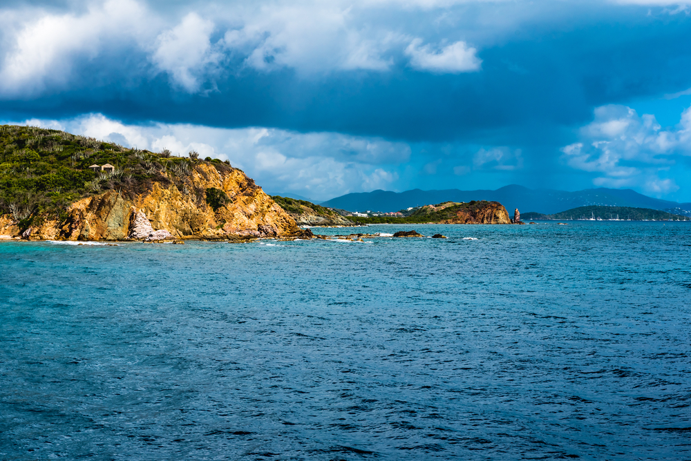Rain clouds and rain above the beach and rock formations along the coast of St. Thomas during the cheapest best time to visit