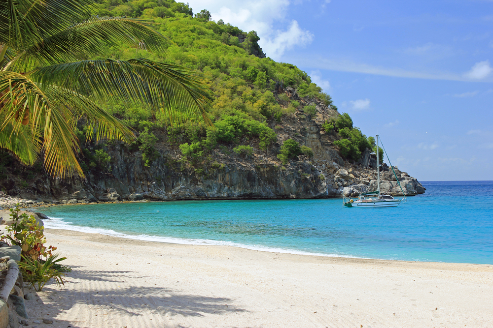 Gorgeous white sand beach in St. Barts surrounded by green trees with a boat moored just off the coast