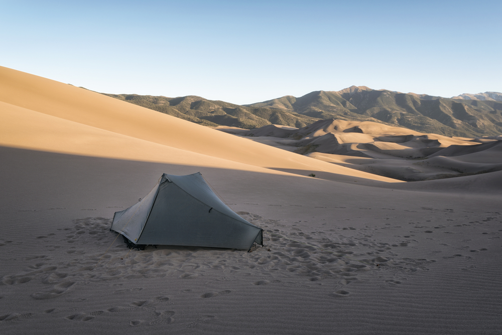 Single camper in a beige tent that's zipped up in the shadows of a sand dune, camping during the least busy time to visit Great Sand Dunes National Park