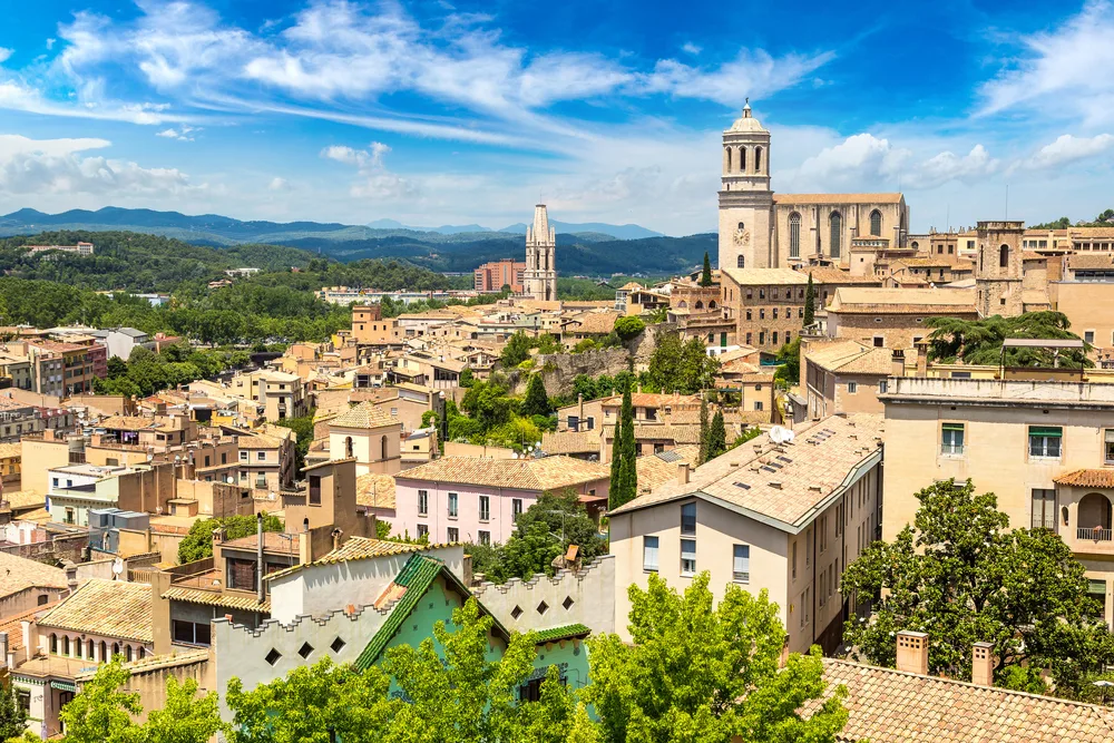 Colorful hillside town of Girona and a cathedral in the middle pictured for a roundup of the best day trips from Barcelona
