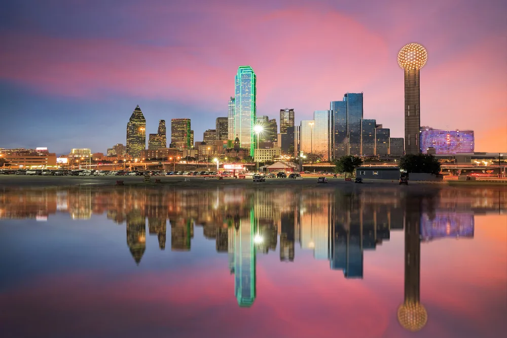 Downtown skyline of Dallas, one of hte best places to visit in the United States, with a tower and buildings reflected on the water