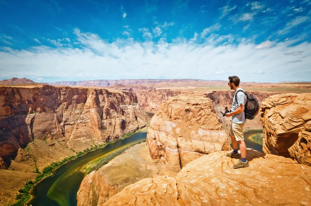 Man in hiking boots holding a camera and looking over the scenic overlook during the best time to visit Horseshoe Bend in Utah