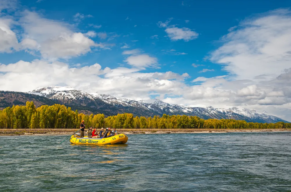 Yellow river raft floating down the Snake River with a big mountain in the background during the best time to visit Jackson Hole, the fall