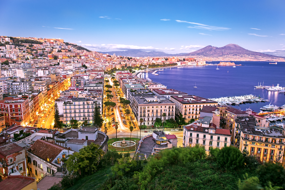Aerial shot of Naples, one of the best day trips from Rome, pictured with yachts in the harbor and a downtown area lining the coast of the water
