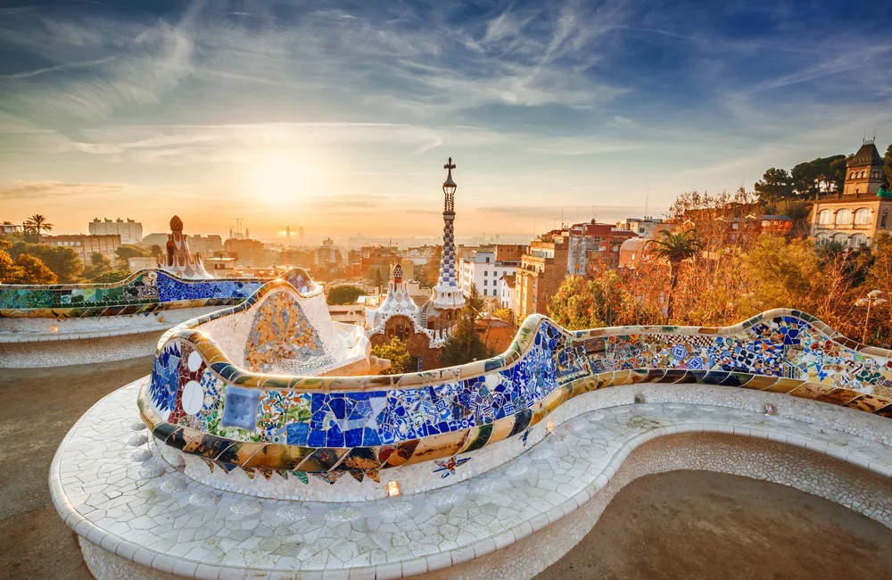 Morning light shines over a park in Barcelona, one of the best places in Spain to visit on a trip, with the colorful park bench snaking around the grounds