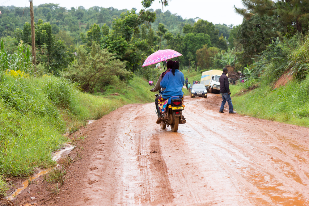 People on bikes making their way down the dirt road on a rainy day during the worst time to visit Uganda
