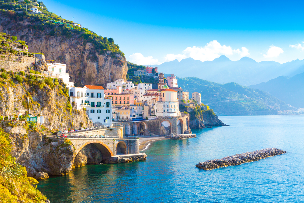 Morning view of blue skies and a few clouds over the cliffside town of the Amalfi Coast, pictured with roads running along the cliffs